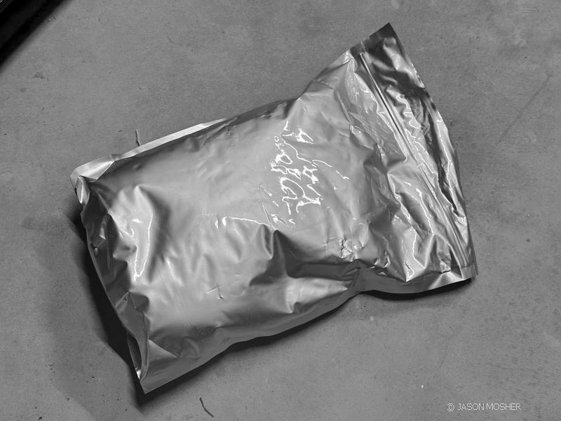 A grey bag of emergency food laying on a dark grey surface. 