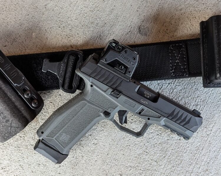 gun, optic, holster, and belt on concrete