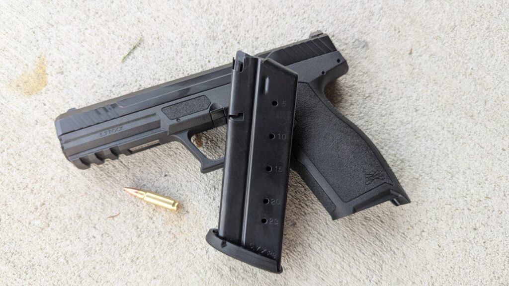 5.7 handgun on concrete, empty mag resting on top of gun, and a single round of ammo