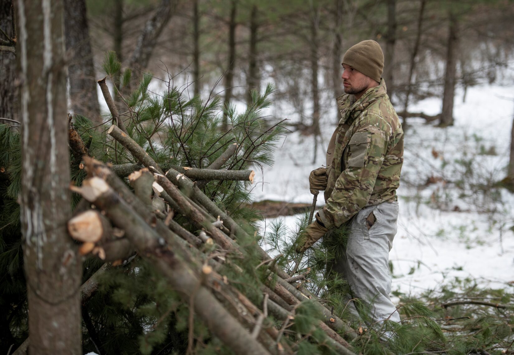 US Army photo of a man building an outdoor shelter with evergreen limbs