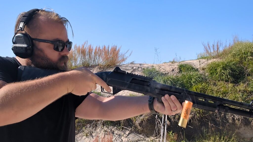 man shooting Benelli shotgun outdoors, shell ejecting and smoke from ejection port is visible.