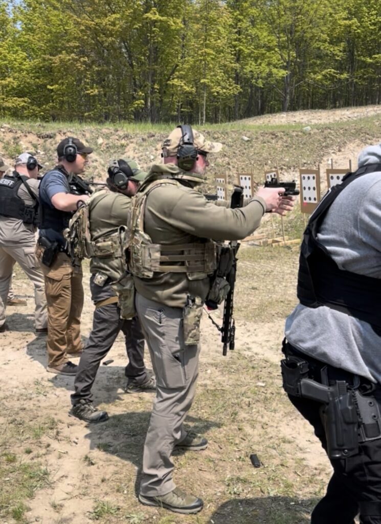A law enforcement officer conducting a carbine to pistol transition on a firing line with other officers wearing body armor