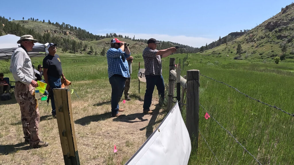 Shooting and iron sight revolver at Handgun Hunters Competition with spotters helping.