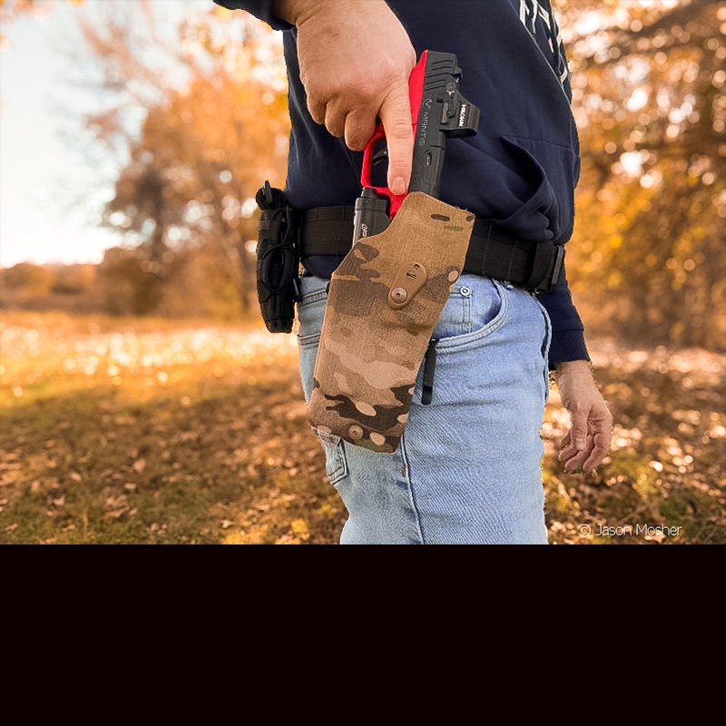 A person in a blue hoodie and jeans, holstering a red and black training pistol.