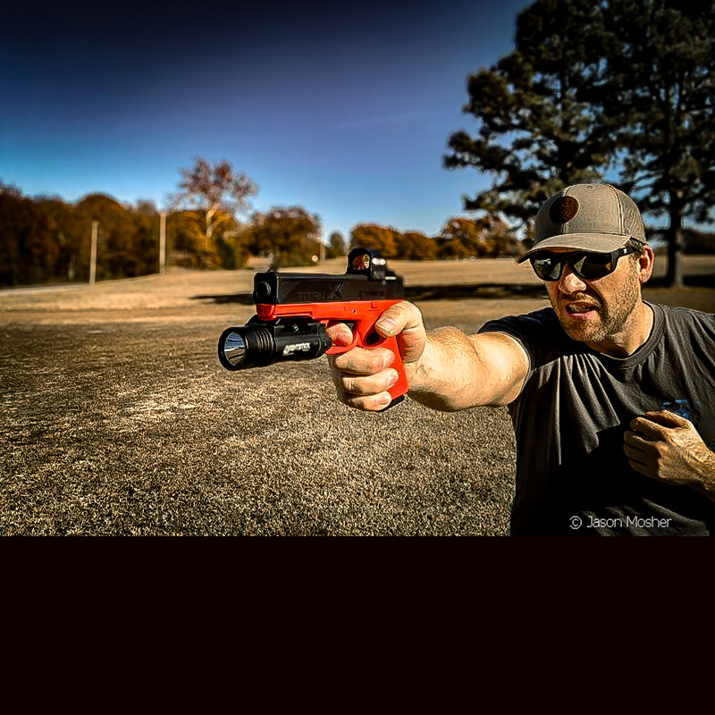 A person in a grey shirt, shooting an orange and black training pistol.