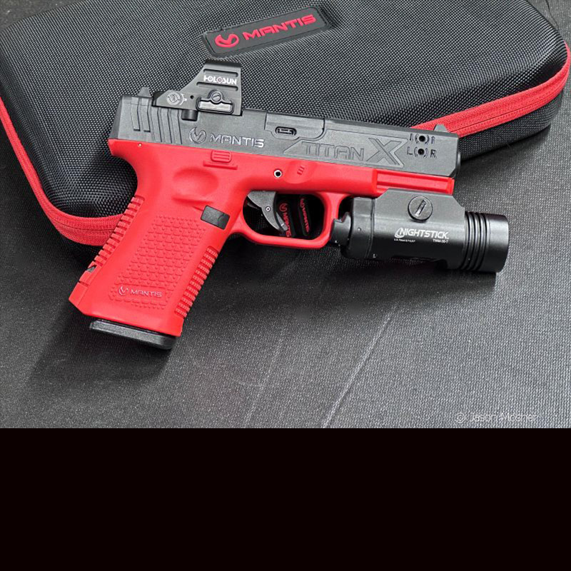 An orange and black training pistol leaning against a black case. Mantis TitanX