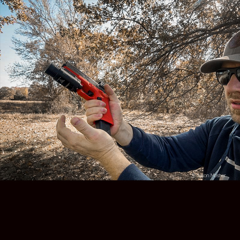 A person holding an orange and black handgun out in front of them while changing the magazine.