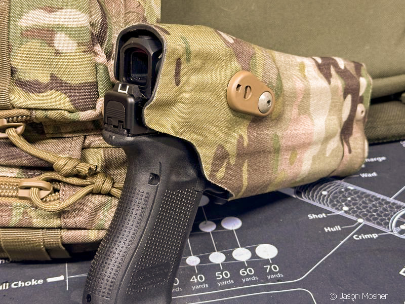 A camouflaged RDSO holster with a black, Glock 19 and enclosed emitter red dot in the holster, sitting on a counter. Safariland acronyms