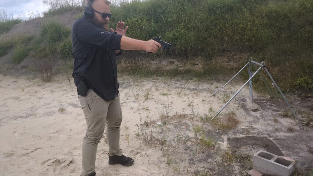 Man aiming handgun with extended arm at outdoor range.