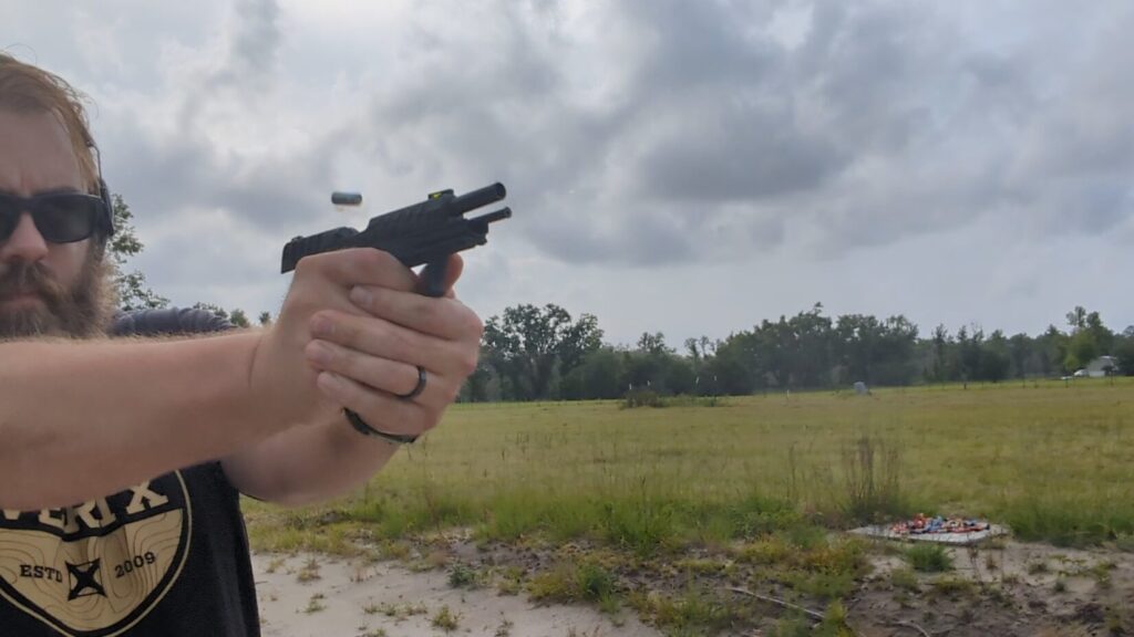 man shooting KelTec P15. Slide is back and empty case is in the air after ejection. Muzzle is lifted, showing the gun's recoil