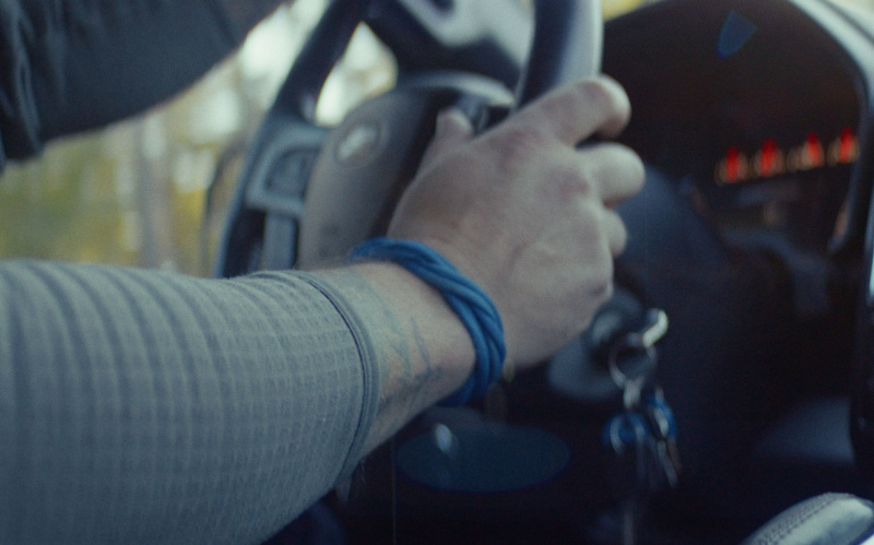 blue cord bracelet on man's wrist - hand on steering wheel