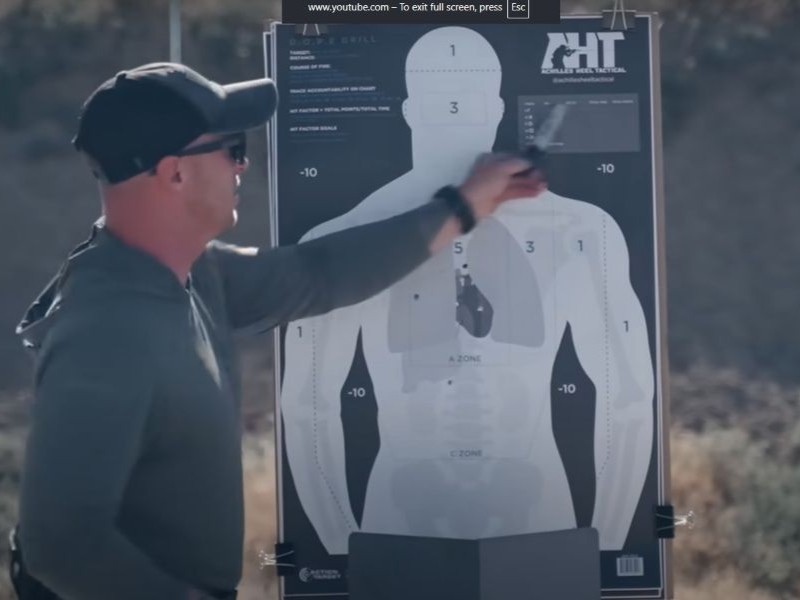 Instructor Rick Crawly stands in front of his target on the range and holds a pen up to one of the holes as he counts his hits. 