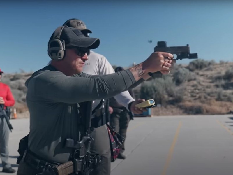 A firearms instructor fires a handgun at a target as the students watch. 