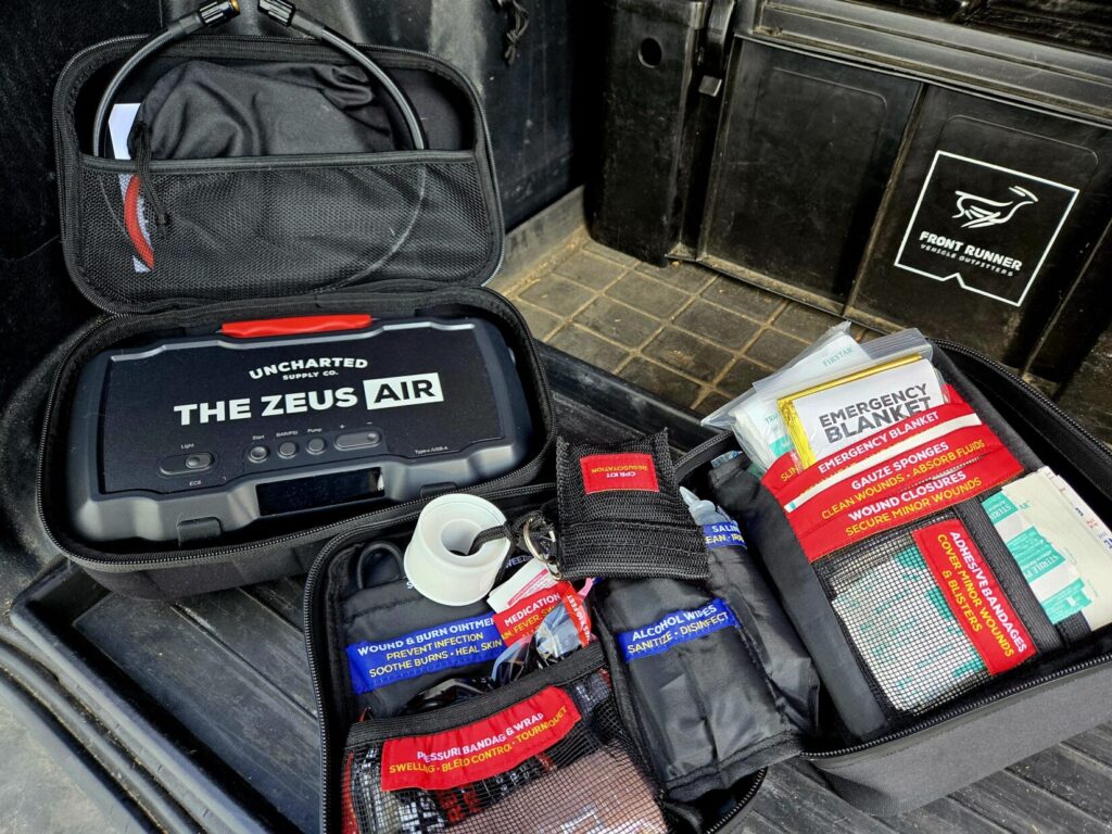 Overlanding gear: An Uncharted Supply Company compressor and battery pack next to a first-aid kit with front runner cargo box in the back of a 4runner.