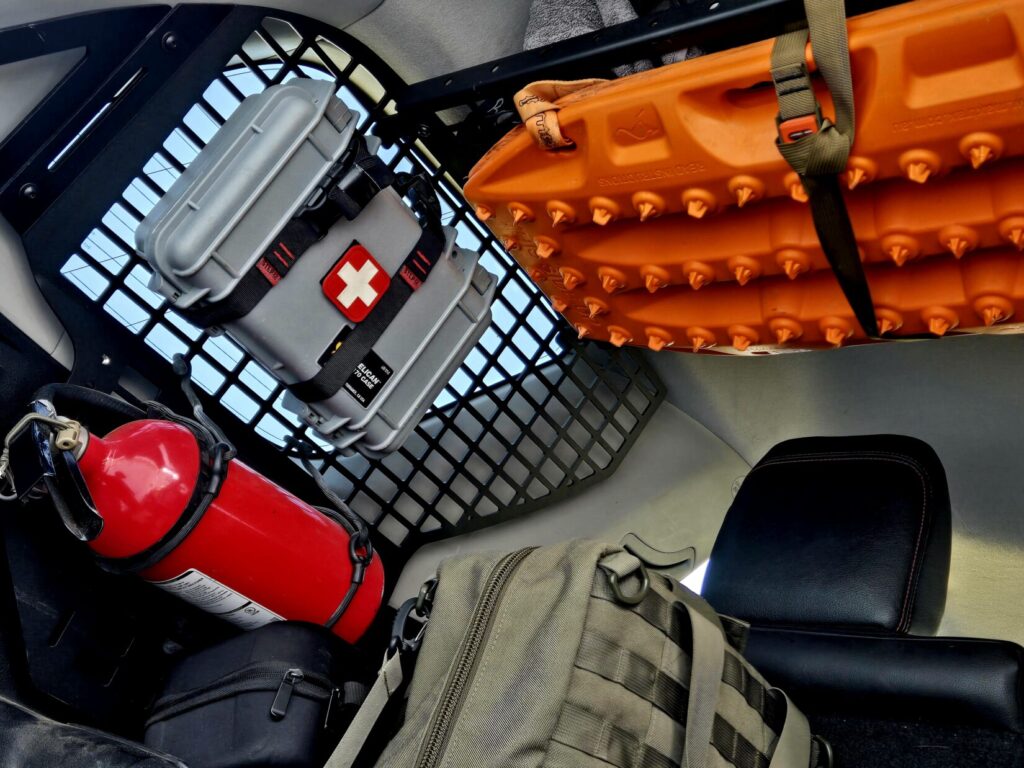 Overlanding gear: Recovery Boards, medical kit, fire extinguisher, and HSGI bag carried in the back of a SUV with MOLLE panel grates.