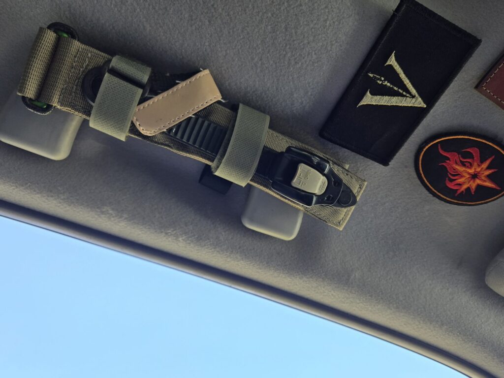 A ratcheting tourniquet is secured to the grab handle of a 4runner with Obsidian Spear Group and Kevin Estela, LLC patches visible