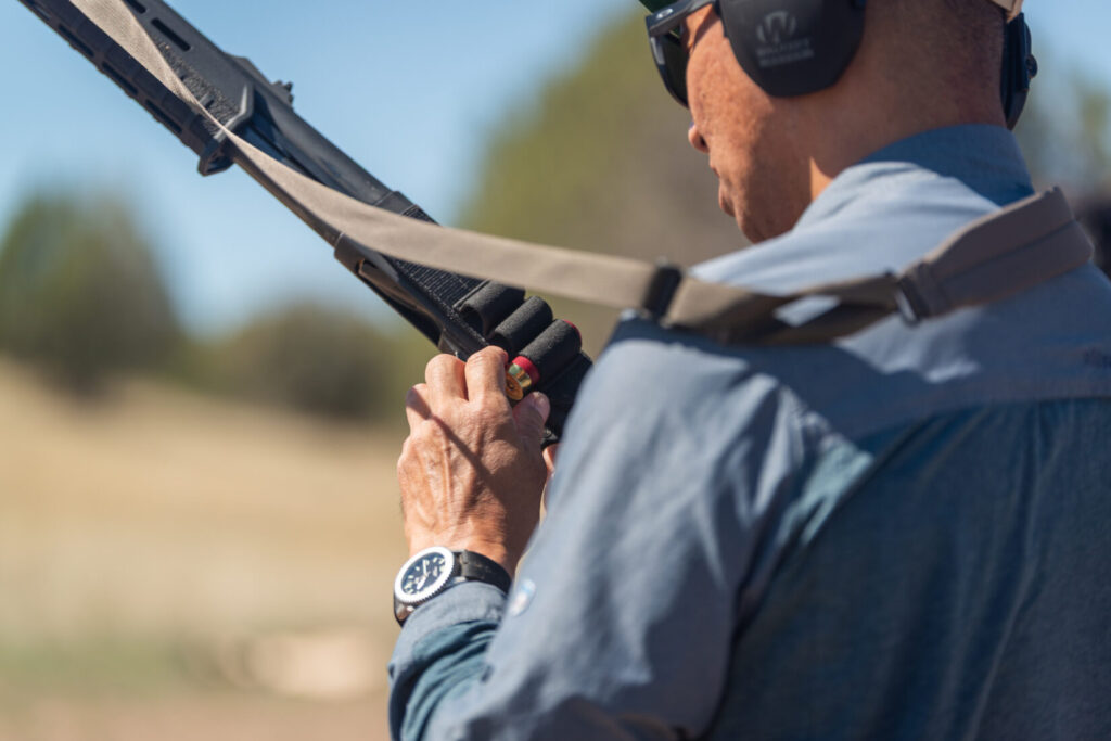 A shotgunner is reaching for a shotgun shell from a side saddle on a Vang Comp Shotgun