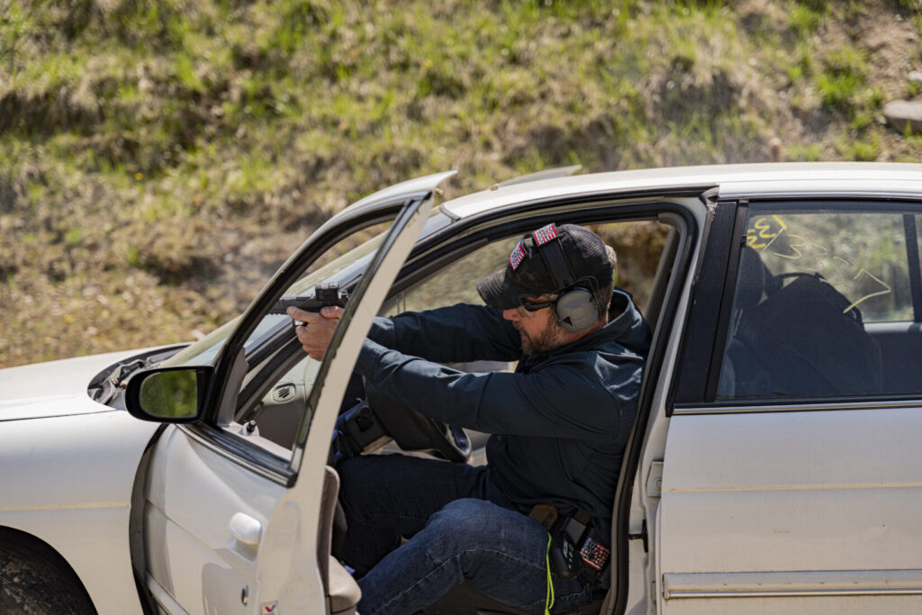 Rick Hogg of War HOGG Tactical is demonstrating to law enforcement officers how to shoot a pistol from a seated position in a vehicle.