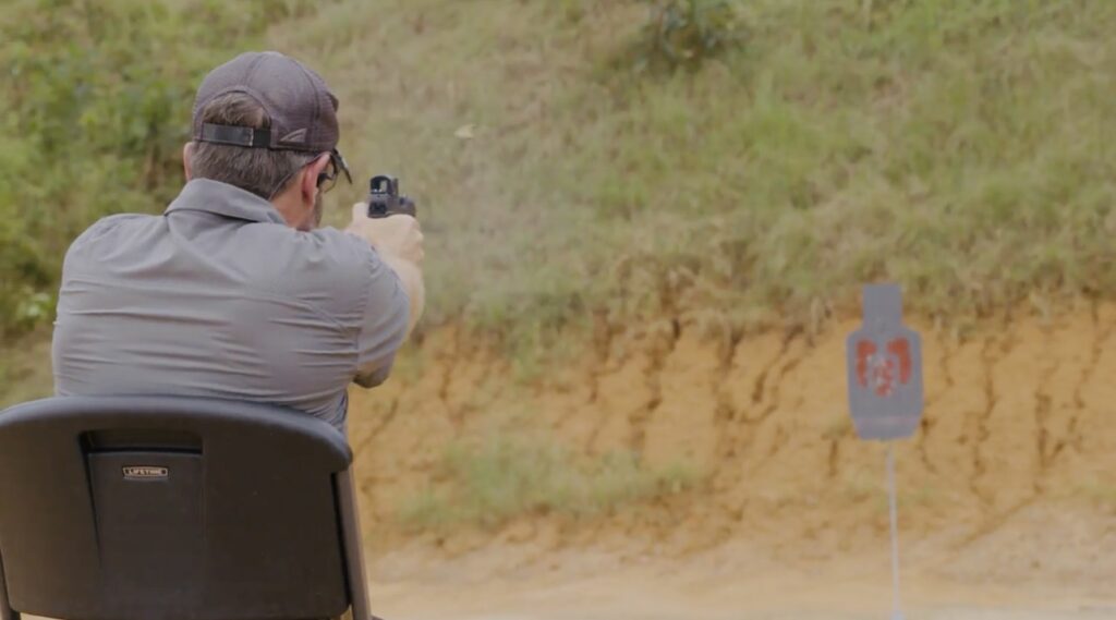 posterior view of Rick Hogg of War HOGG Tactical shooting a steel target with his pistol while in a seated position 
