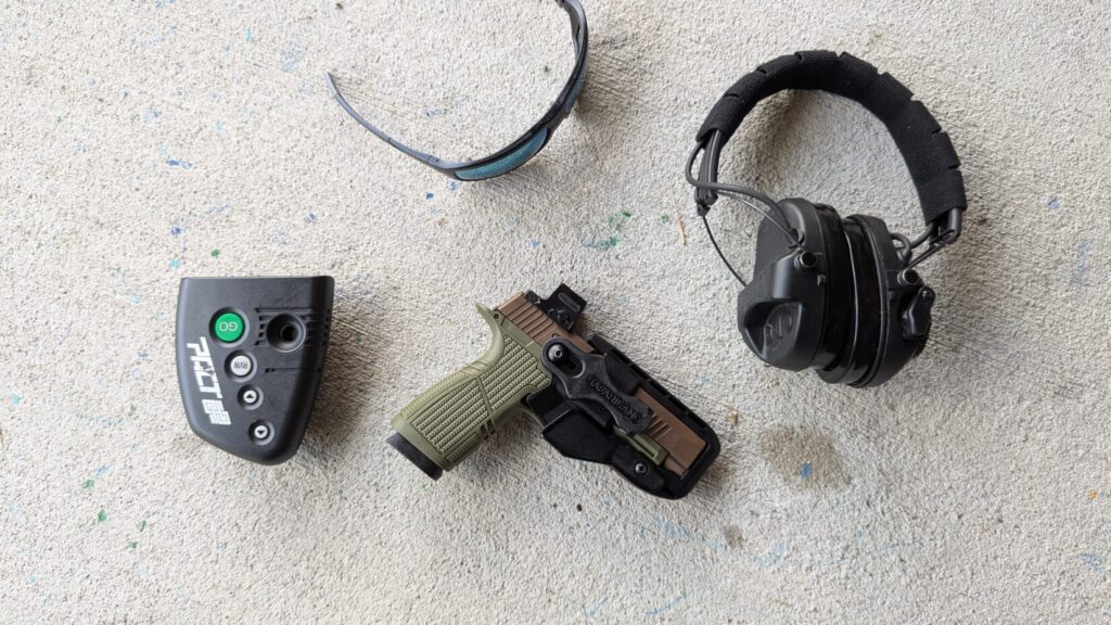 Pistol in holster, shot timer, eye protection, and ear protection.