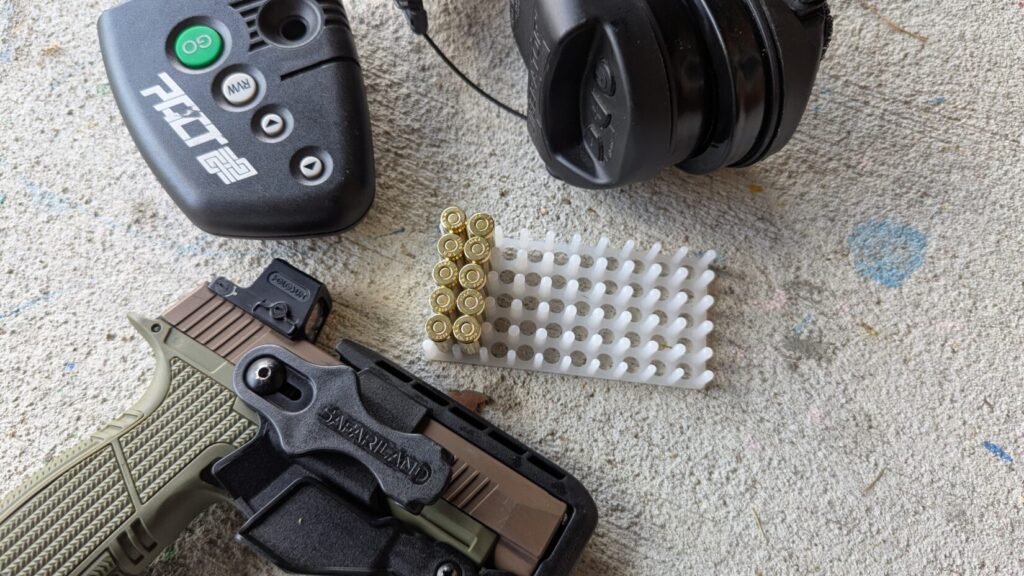 Pistol in holster, shot timer, ear protection, and ammunition in a tray.