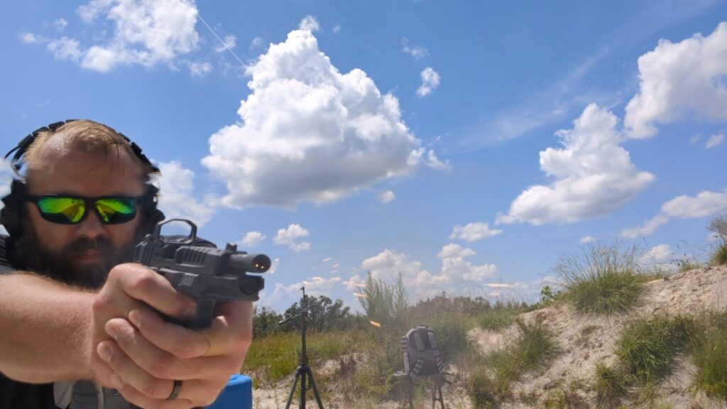 Man firing Echelon pistol, muzzle flash visible.