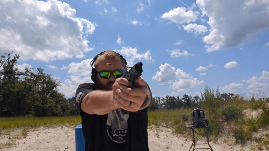 Man firing Echelon pistol, spent casing in air.