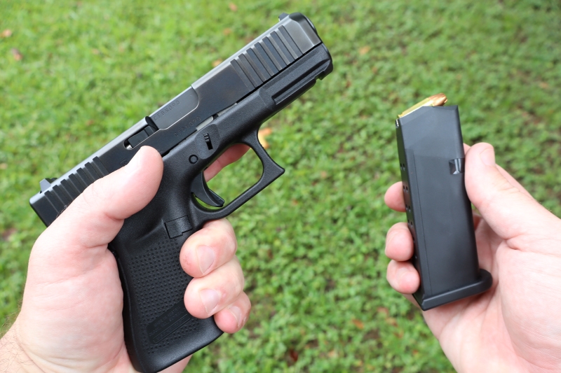 glock 19 gen 5 pistol  in left hand and fifteen round magazine in right hand. Grassy bacground