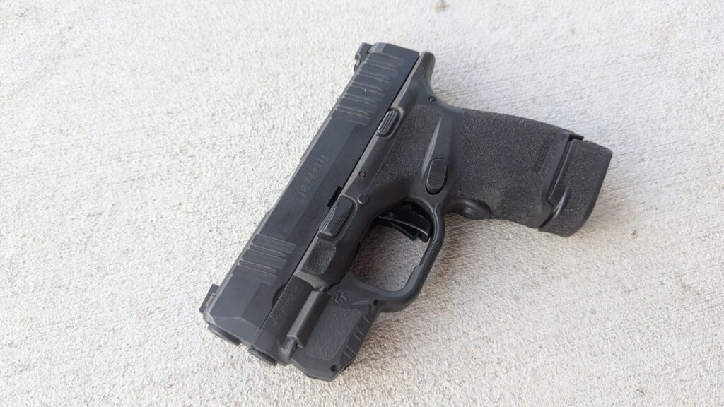 Black Hellcat pistol with tactical light attached, resting on concrete.