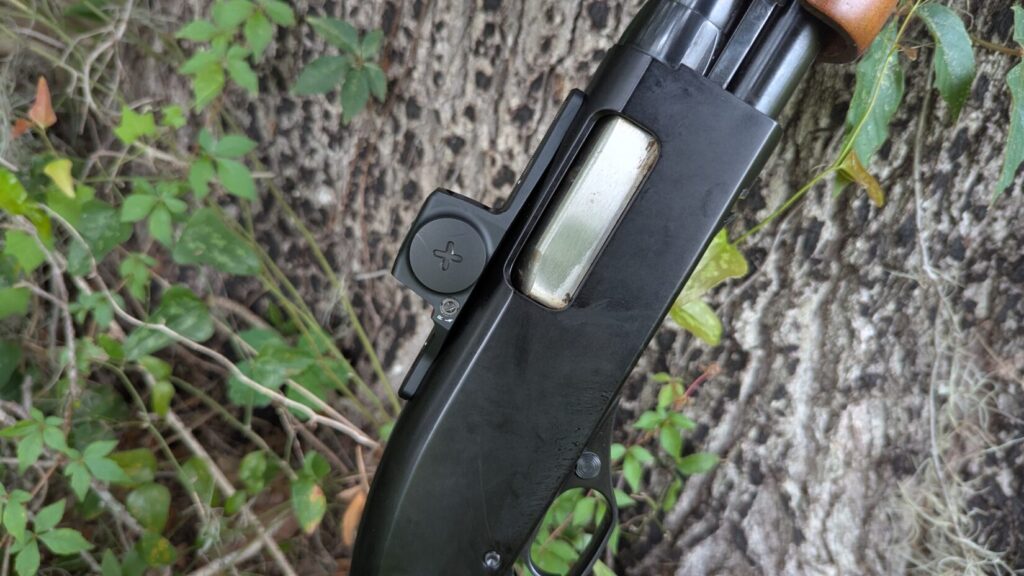 Side view of a shotgun with a Vortex Viper red dot sight, against a tree.