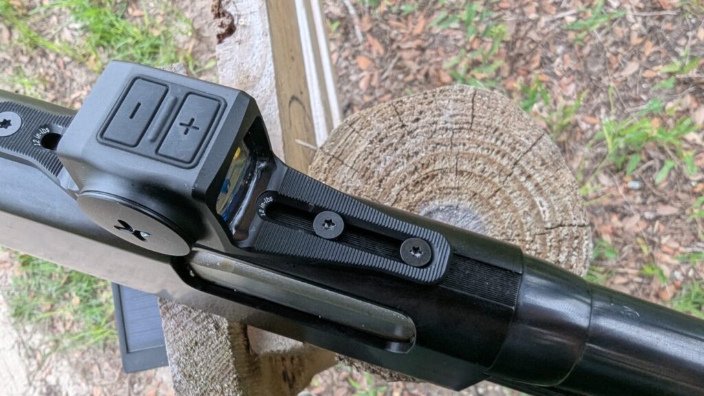 Close-up side view of a red dot sight mounted on a shotgun, showing elevation adjustment.