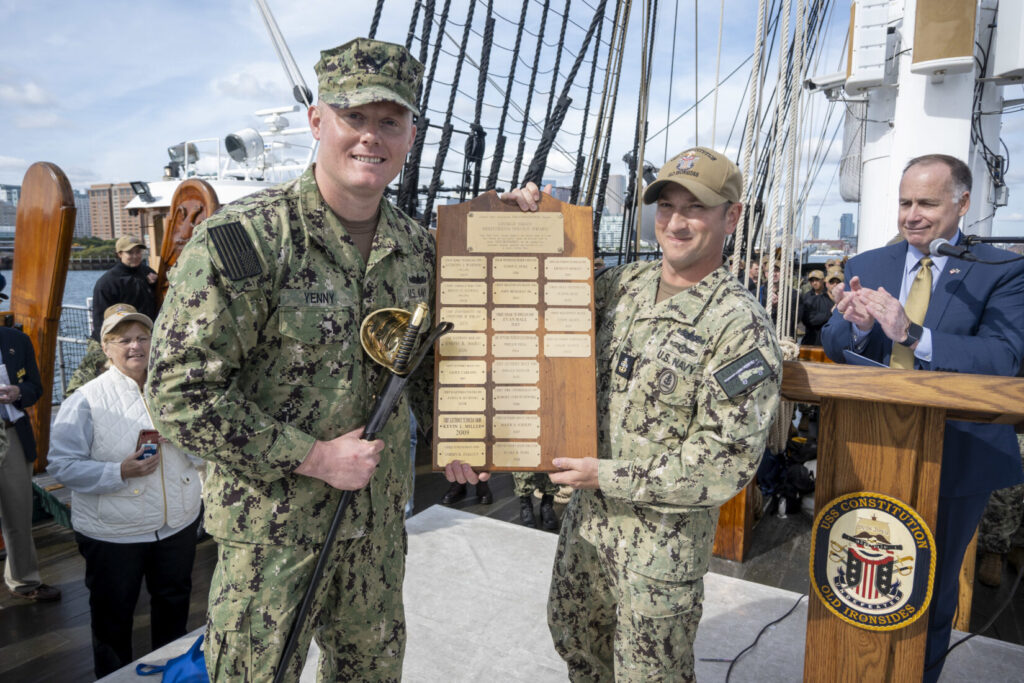 Command Senior Chief Seth Miles, right, presents Chief Gas Turbine Systems Technician (Mechanical) Adam Yenny with the 2021 USS Constitution George Sirian Meritorious Leadership Award plaque while underway aboard USS Constitution. (U.S. Navy Photo by Mass Communication Specialist 1st Class Grant G. Grady/Released. PublicDomain)