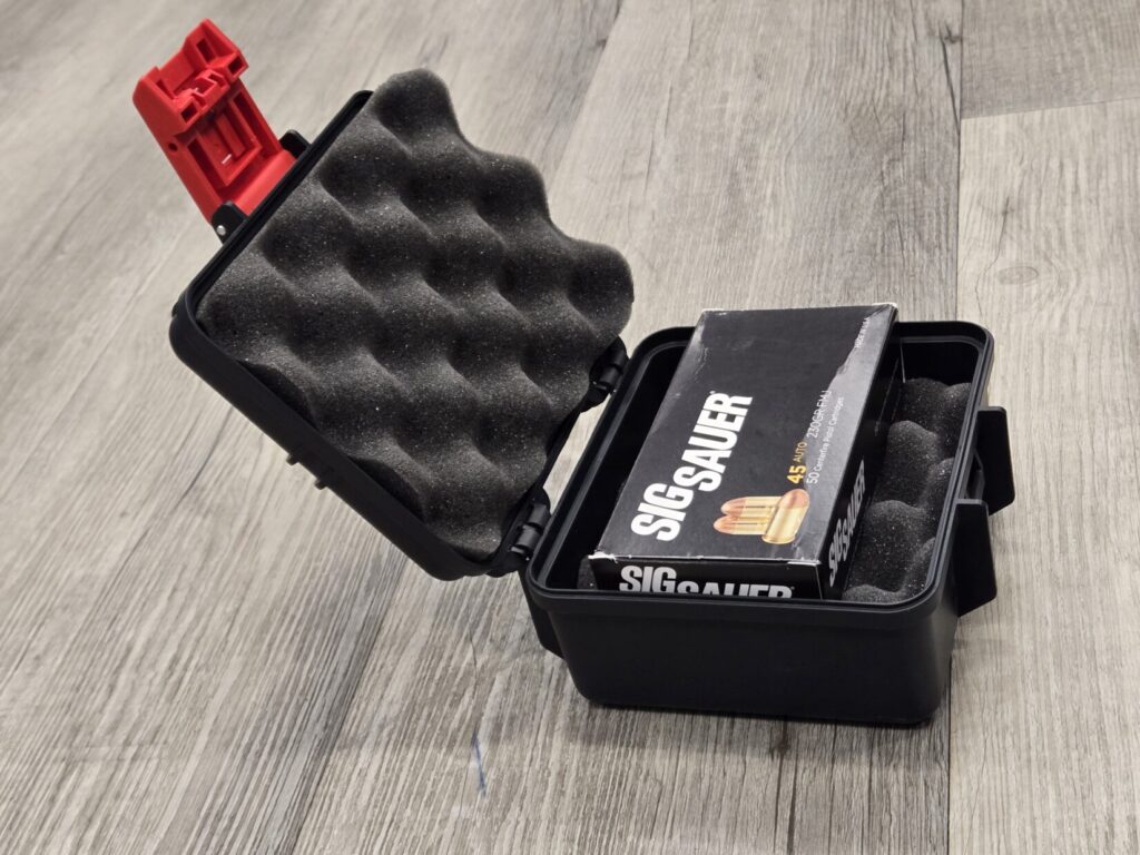 A small padded black box with a red latch holding a box of ammunition