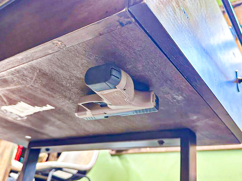 A brown handgun stuck to the bottom of a drawer using a gun magnet. 