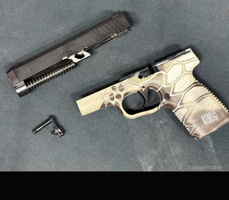 A Kahr SW9 on a black rubber mat with the slide removed from the frame. 