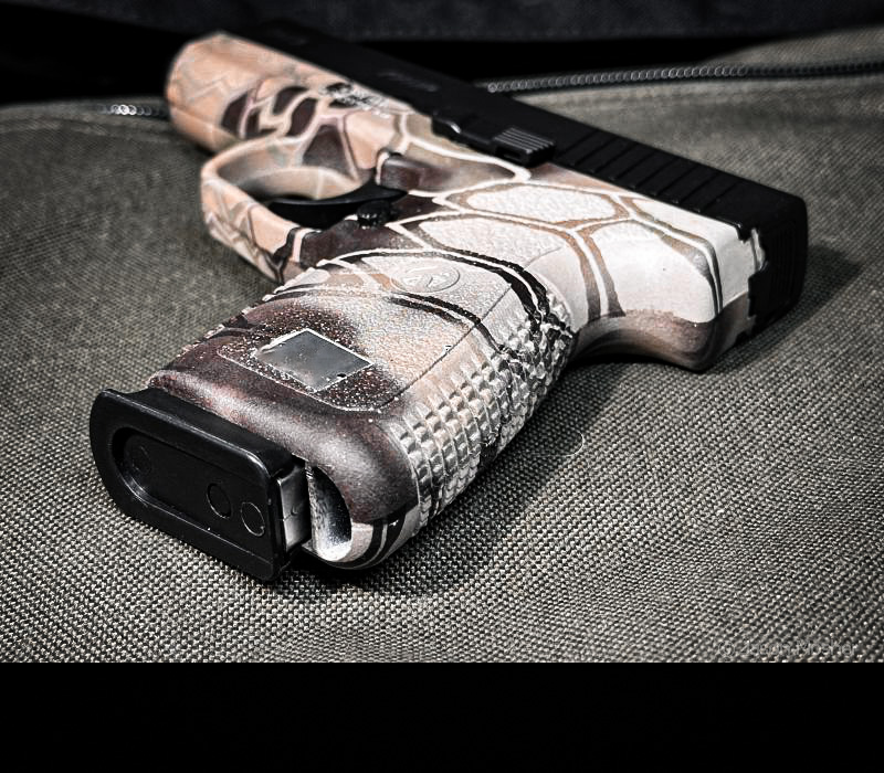 The Kahr SW9, light brown camo handgun with a black slide on a green canvas with the grip portion of the gun facing the camera. 