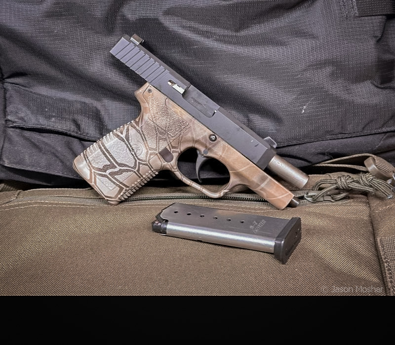 The CW9 handgun with the slide locked open and the magazine lying beside it. The gun is on a green canvas bag with a black background behind it.  