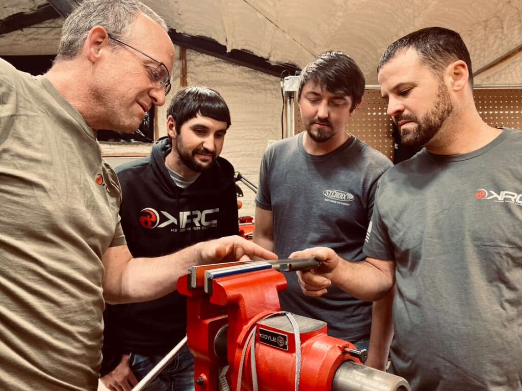 four Kings River Custom gunsmiths stand over a vice holding a 1911 part