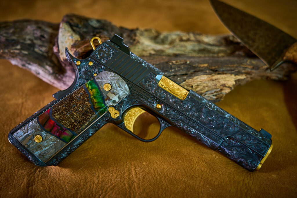 Hand engraved custom 1911 pistol with exotic grips on top of a suede backdrop.