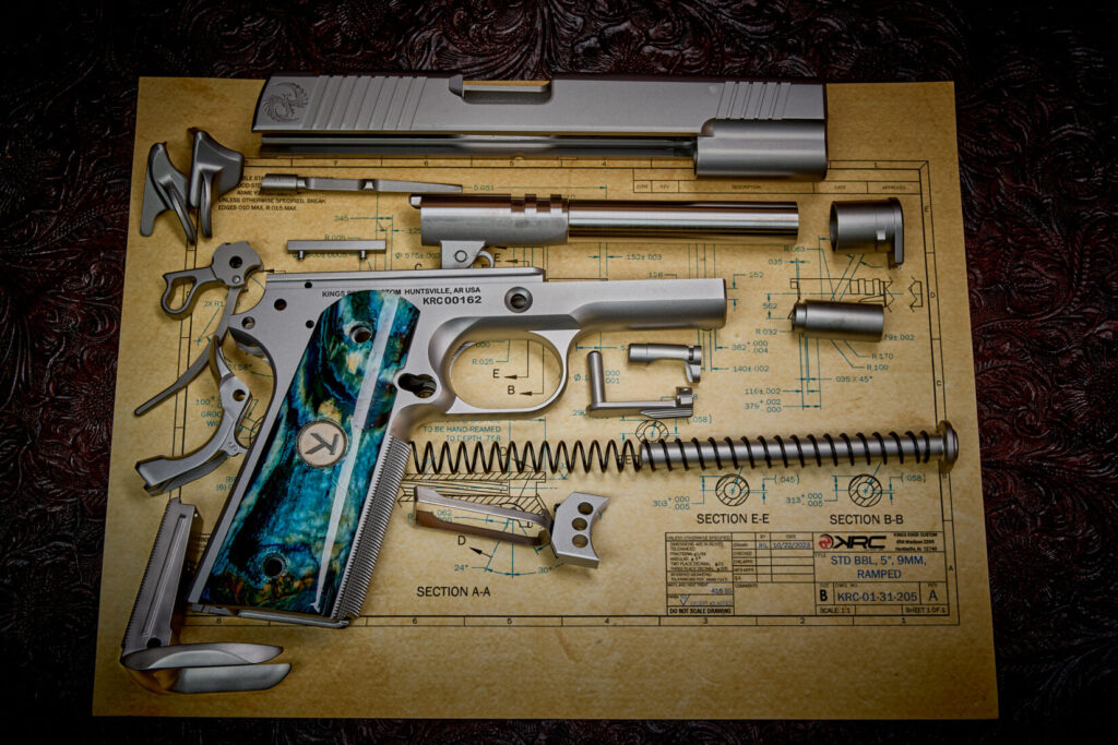 A disassembled 1911 pistol on top of the a blueprint for a 1911.