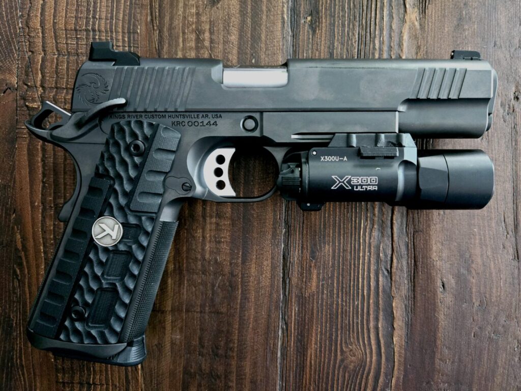 A Kings River Custom 1911 pistol with a surefire x300 ultra light on a wooden backdrop