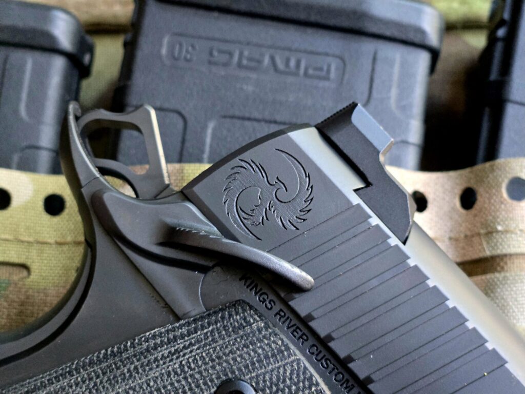 A closeup shot of a 1911 hammer and safety and the logo of Kings River Custom on top of a multicam pouch with pmags in it.