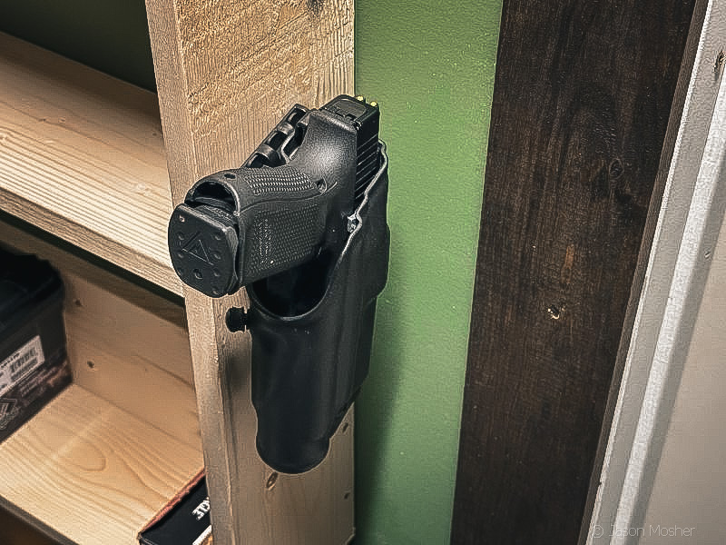 A Safariland holster, holding a Glock 19, attached to the wall in a closet using a QLS mounting system. 
