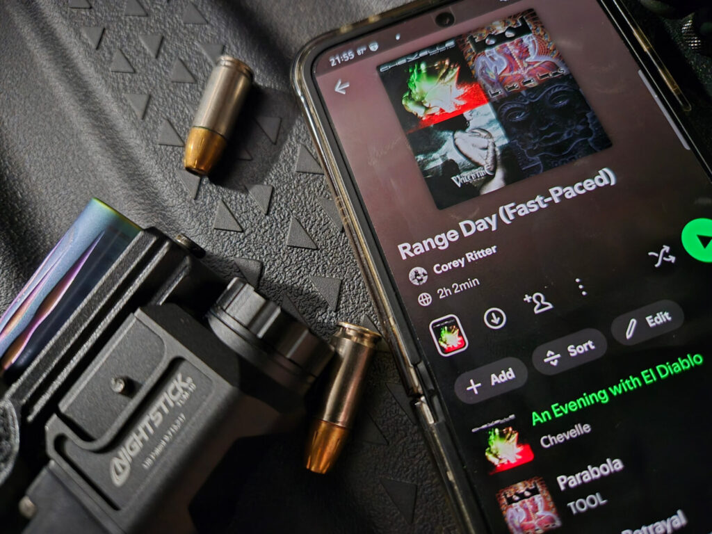 a phone with a spotify playlist open and a gun with ammunition against a black background