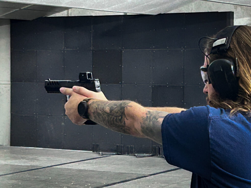 Man at a shooting range firing an optics-ready handgun.