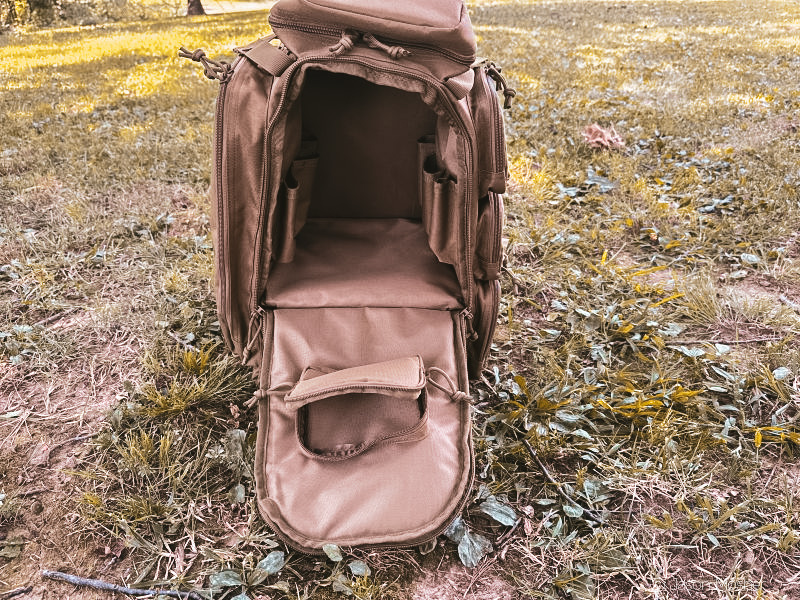 A brown backpack on the ground with the center compartment unzipped and open.