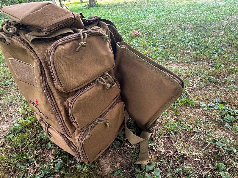 A brown backpack on the ground with the back unzipped, showing the soft pistol case that comes with it and can be stored in the back compartment.
