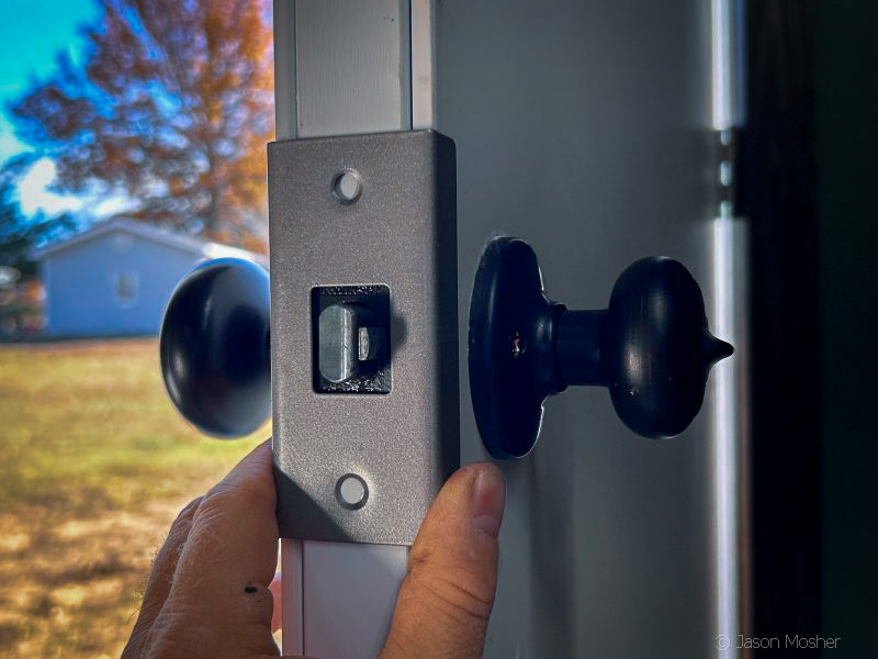 A metal door with a metal brace placed over the locking mechanism by the doorknob. 