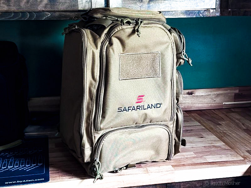 A large brown backpack with multiple external pouches sitting on a counter. The word "Safariland" is printed across the bag in red. 