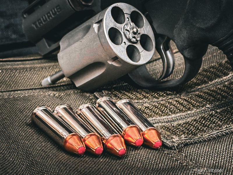 The Taurus 605 Protector Poly revolver sitting on a table with the cylinder open and 5 rounds of Hornady Critical Defense ammo next to it. 
